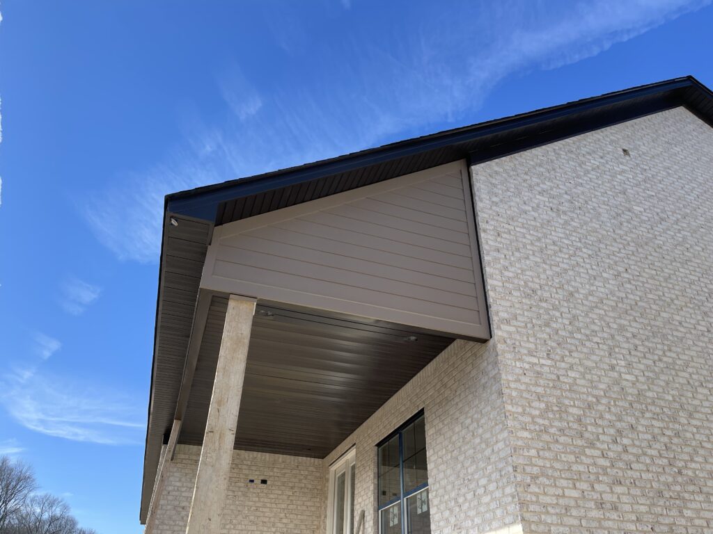 A closeup view of a house's exterior, featuring the ceiling of a porch of a brick house