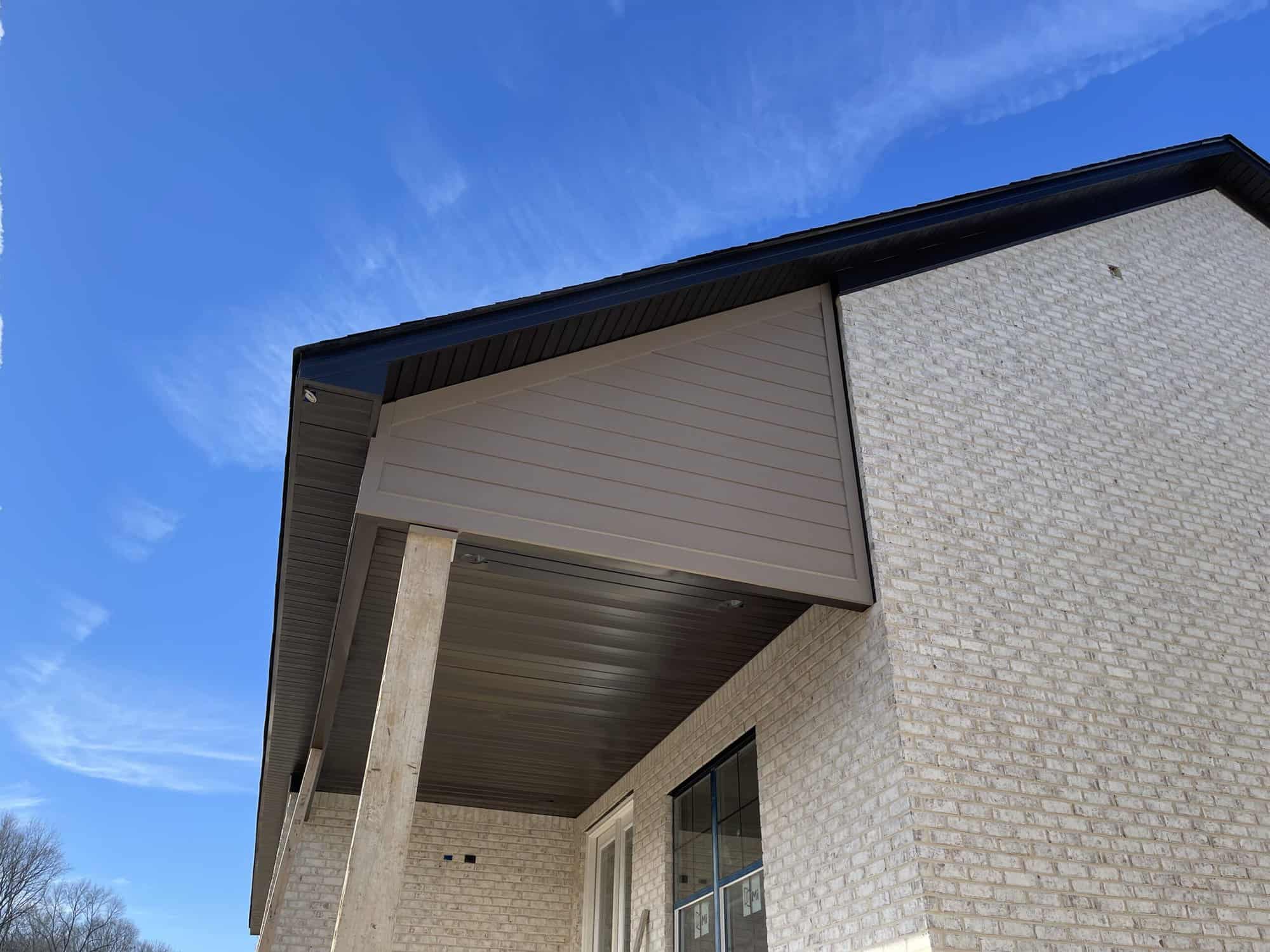 A closeup view of a house's exterior, featuring the ceiling of a porch of a brick house